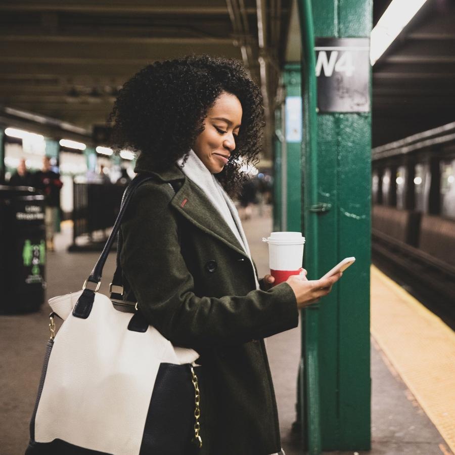 woman with a cup of coffee texts on subway station platform